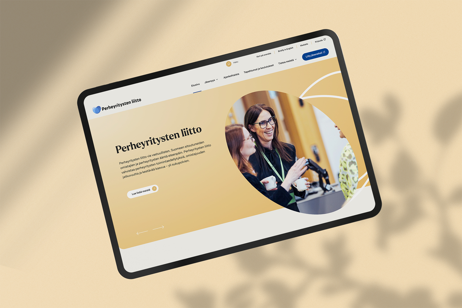 Tabletin näytöllä näkyy Perheyritysten liiton verkkosivuston etusivu ja kuva keskustelevista ihmisistä